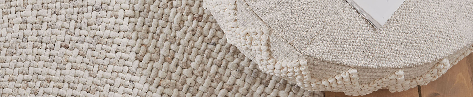 Gewebter Teppich liegt unter rundem Hocker mit Textur und Buch auf Holzboden.