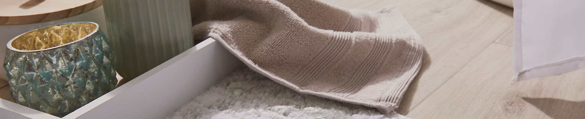 Zwei dekorative Kerzenhalter stehen neben einem offenen weißen Schubfach mit Handtuch auf Boden.