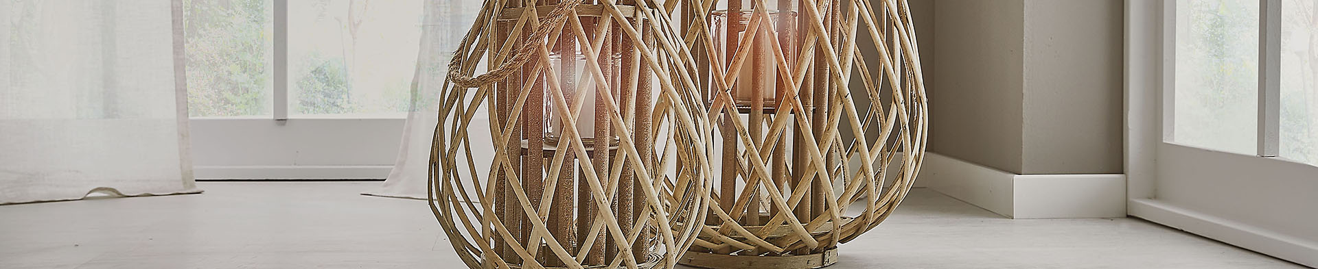 Zwei geflochtene Körbe stehen auf hellem Boden vor großen Fenstern mit weißen Vorhängen.