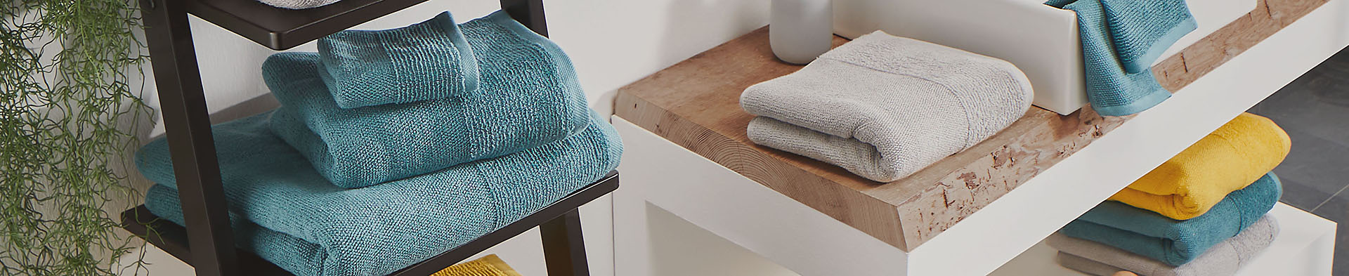 Blau- und graue Handtücher liegen gestapelt auf einem Regal und einer Holzablage im Bad.