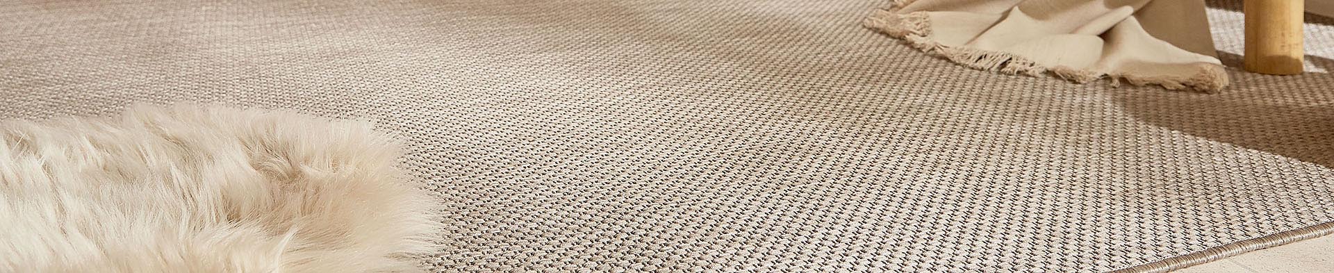 Beiger Teppich liegt auf Boden, links liegt ein Fellteppich, rechts ein beiger Deckenrand sichtbar.