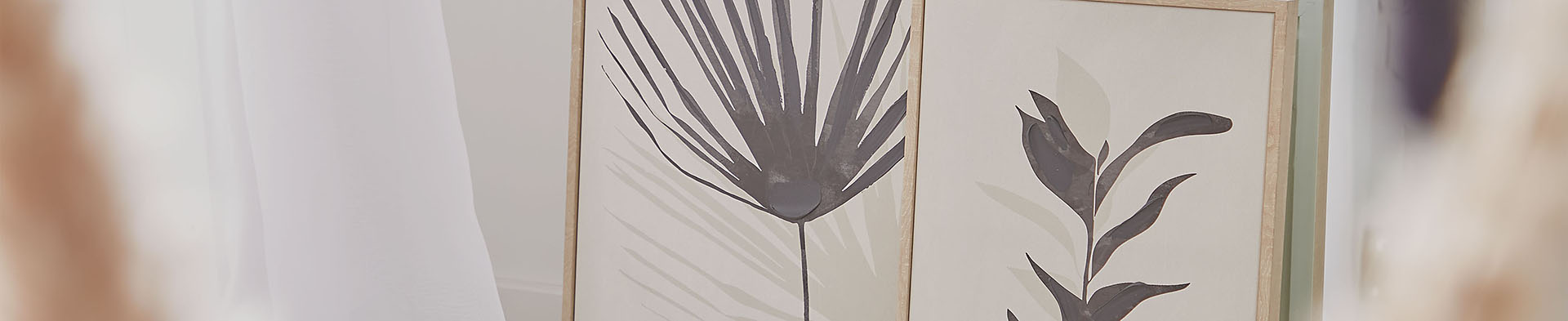 Zwei gerahmte Pflanzenzeichnungen lehnen an einer weißen Wand in einem hellen Raum.