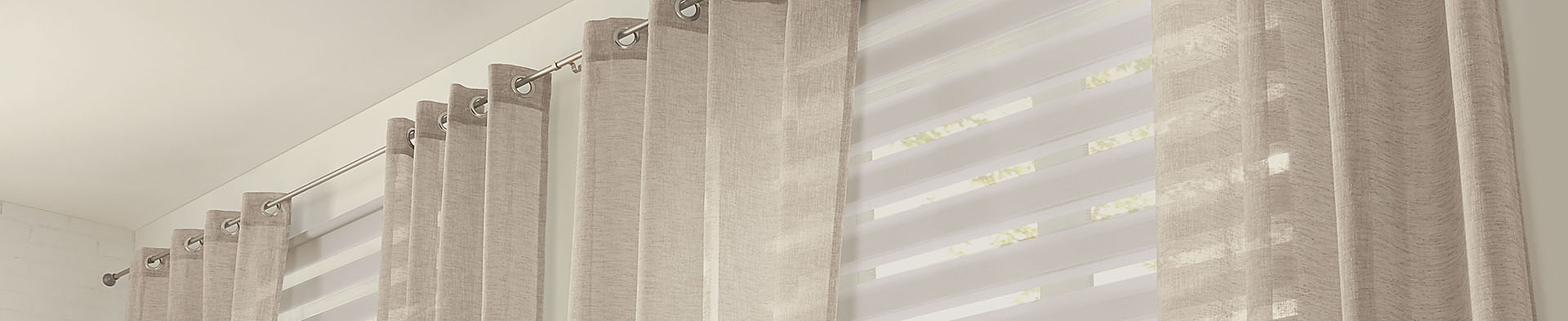 Vorhang hängt an Gardinenstange vor Fenster mit Jalousien in hellem Raum.