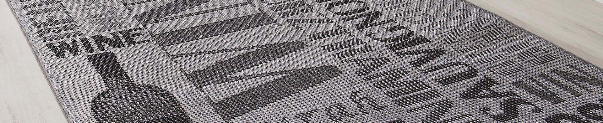 Teppich zeigt Weinflasche und Wörter wie „WINE“, „RED“, „CHAMPAGNE“ auf hellem Boden.