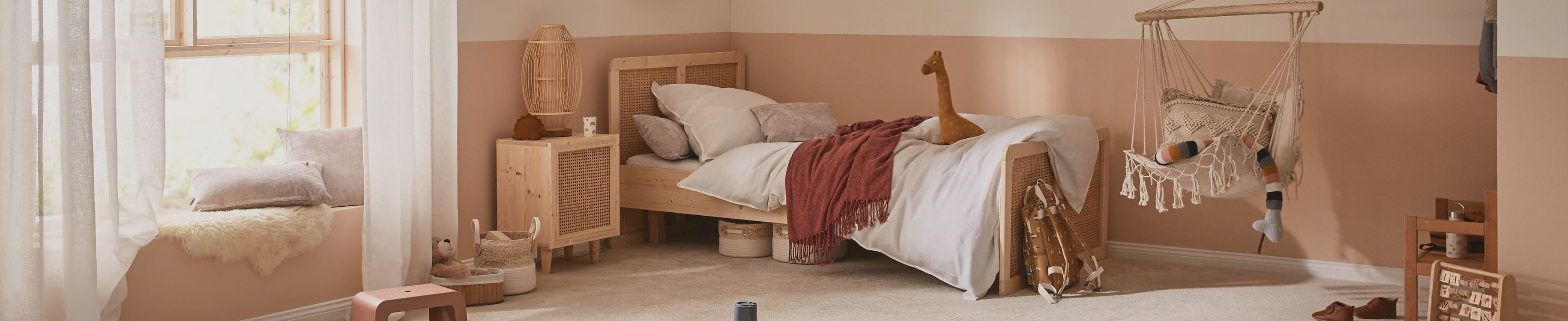 Kinderbett mit Kuscheltier liegt in warmem Zimmer mit Schaukelstuhl und Sitzfenster.