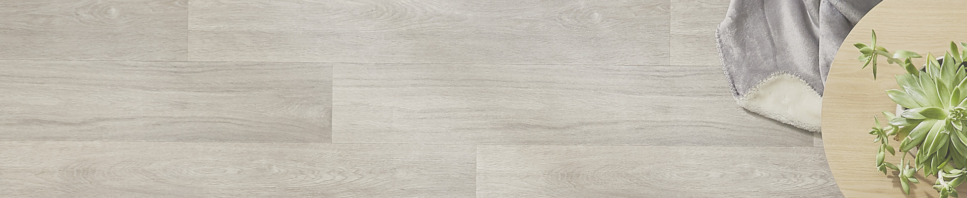 Runder Holztisch mit grünem Sukkulentenpflanze, graue Decke auf hellem Boden.