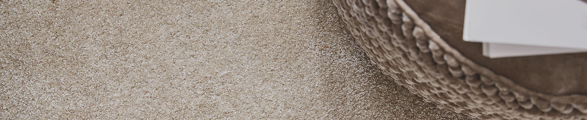 Beiger Teppich bedeckt Boden, runder gemusterter Hocker mit Stapel Papier liegt rechts oben.