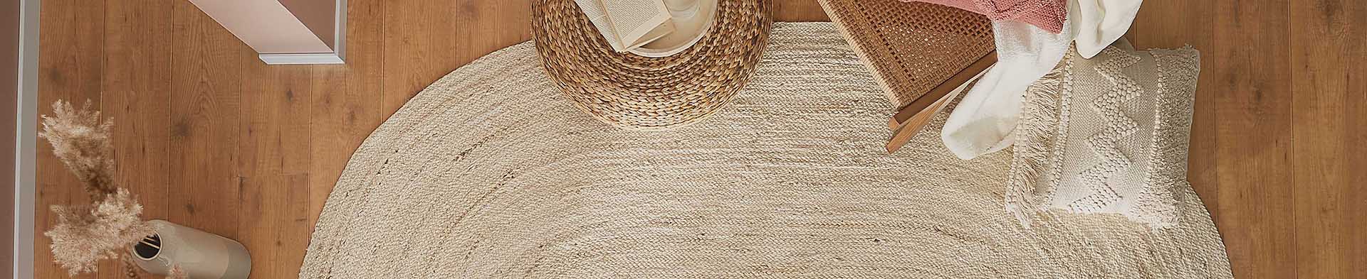 Runder Teppich liegt auf Holzboden, daneben Sessel mit Kissen und Korb mit Buch.