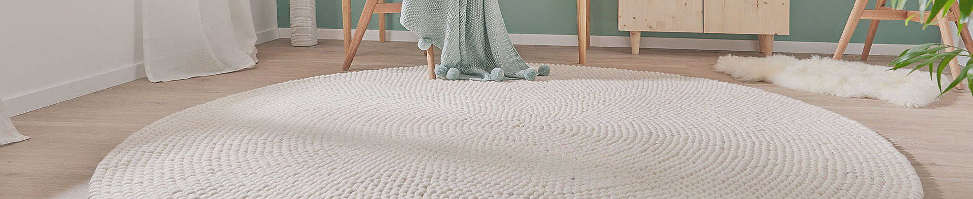 Runder weißer Teppich liegt auf Holzfußboden in Zimmer mit Stuhl, Decke und Möbeln.