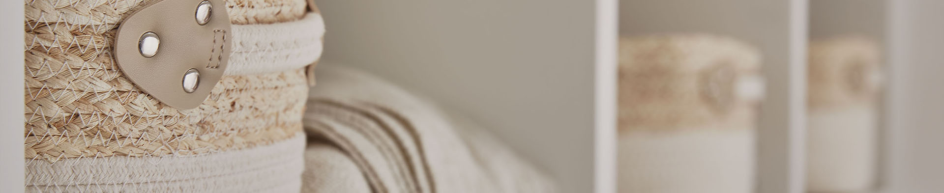 Geflochtener Korb mit angenähtem Ledergriff, dahinter gefaltete Decke in Regalfach.