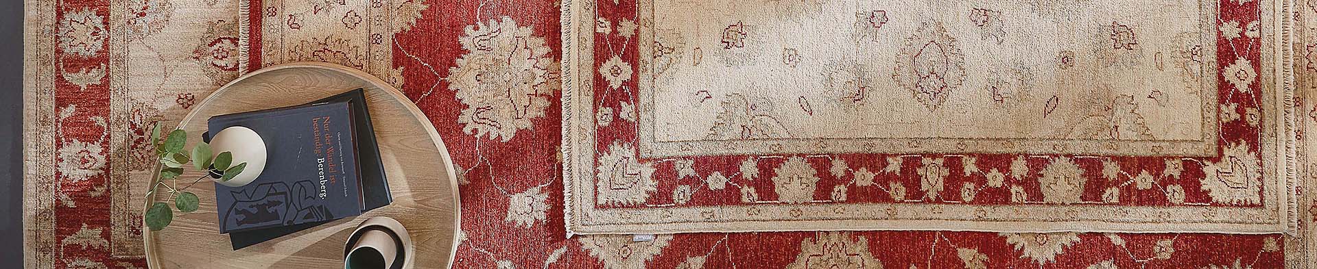 runder Holztisch steht auf Teppich mit Bücher und Pflanze in Vase