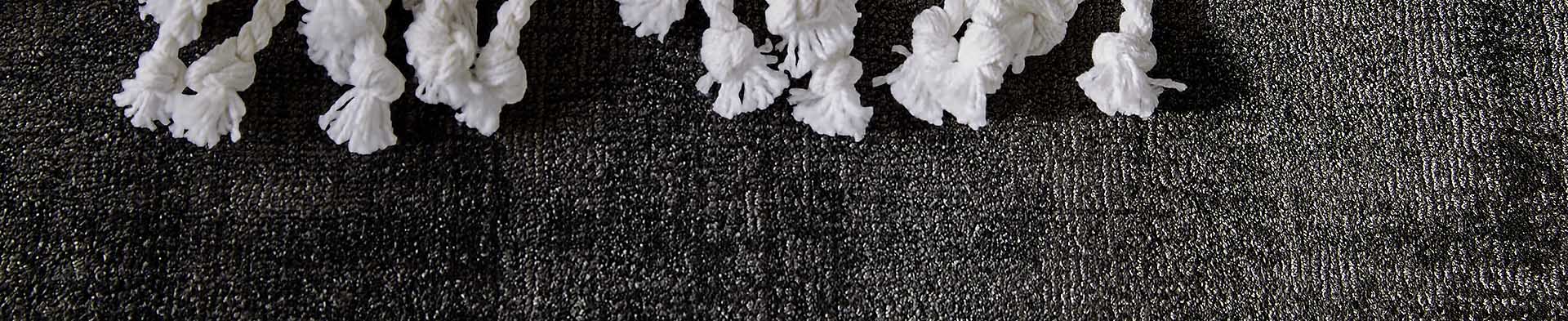 Weiße Kordelenden mit Fransen liegen auf einer dunklen, strukturierten Oberfläche.
