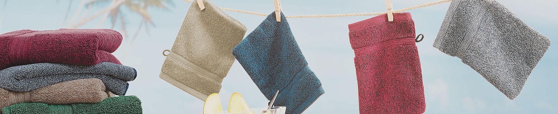 Mehrfarbige Waschhandschuhe hängen an einer Wäscheleine im Außenbereich mit klarem Himmel.