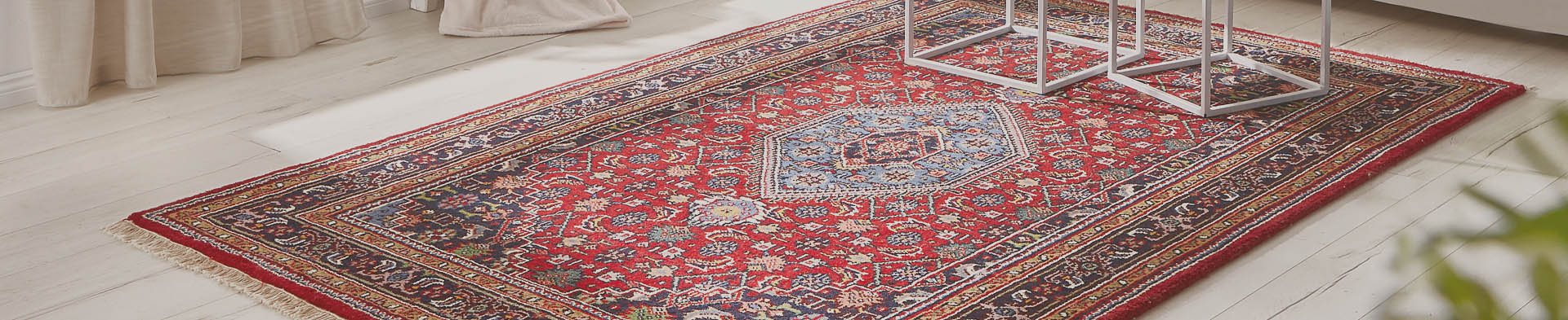 Roter Teppich mit blauem Mittelmotiv liegt auf hellem Holzboden in hellem Raum