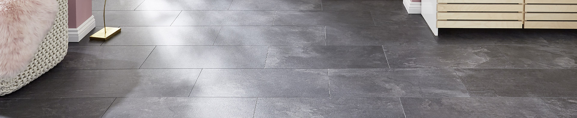 Bodenfliesen liegen glatt und dunkelgrau im Raum mit Möbeln und rosafarbenen Wänden.