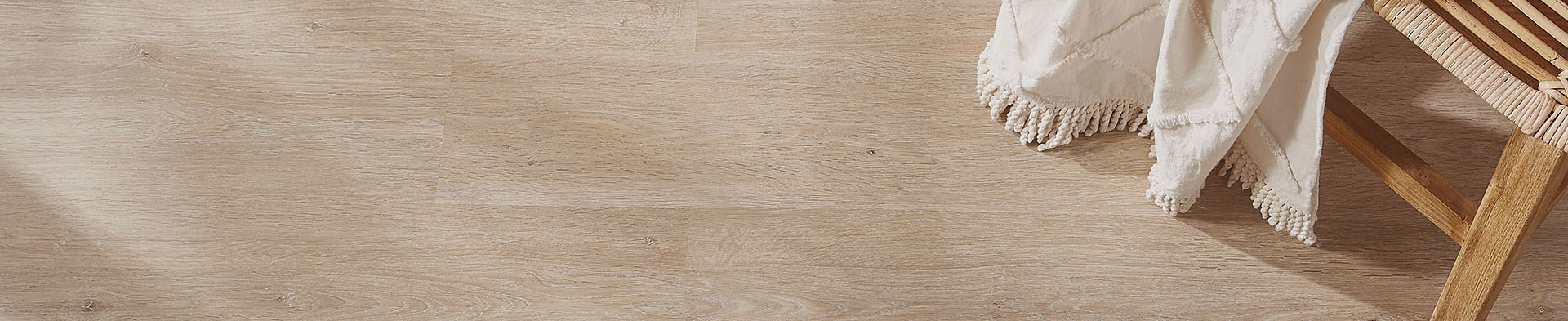 Holzstuhl steht auf hellem Holzboden, mit beige Decke mit Fransen darüber gelegt.