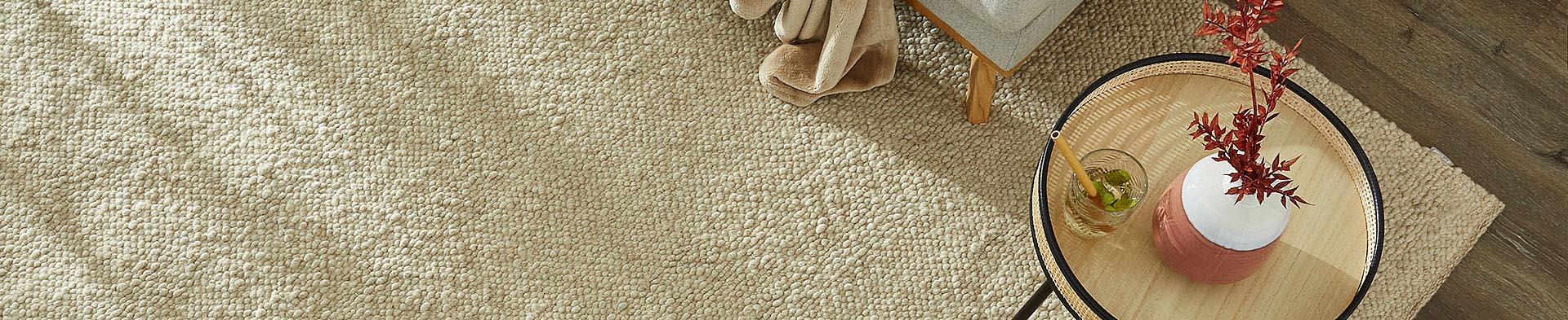 Runder Tisch mit Glas und Vase auf beigem Teppich vor Stuhl auf Holzboden.