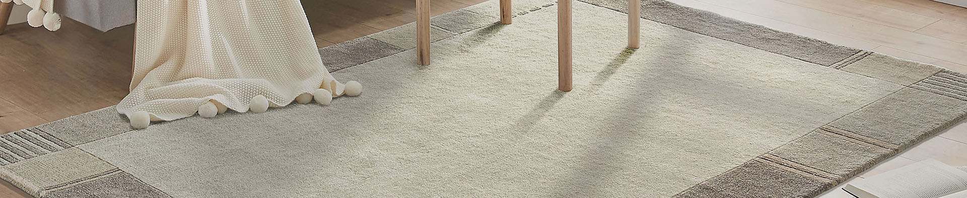 Teppich liegt auf Holzboden, Decke mit Bommel liegt teilweise auf dem Teppich, Stuhlbeine stehen darauf.