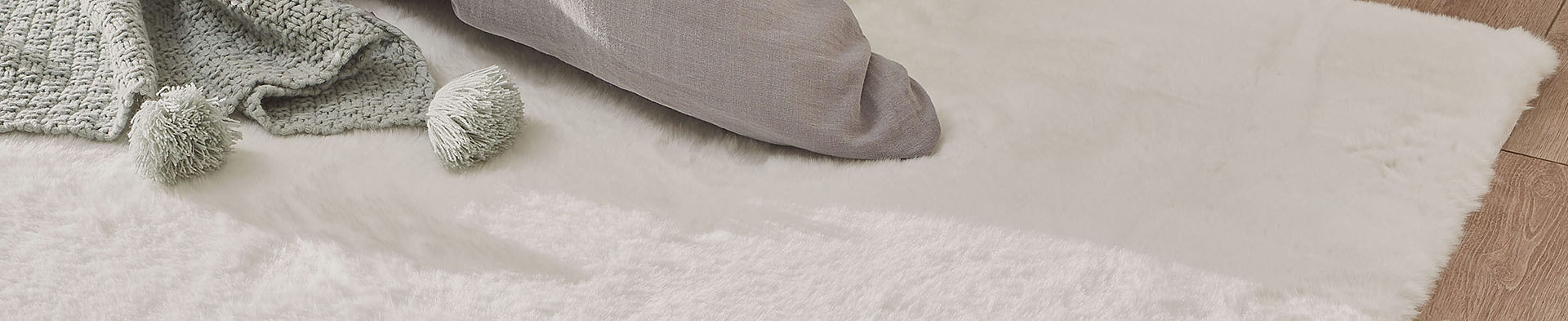 Weicher Teppich mit grauer Decke und grauem Kissen auf hellem Boden in Innenraum