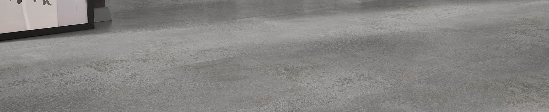 Grauer Boden mit leicht strukturierter Oberfläche vor teilweisem Blick auf einen Bilderrahmen.