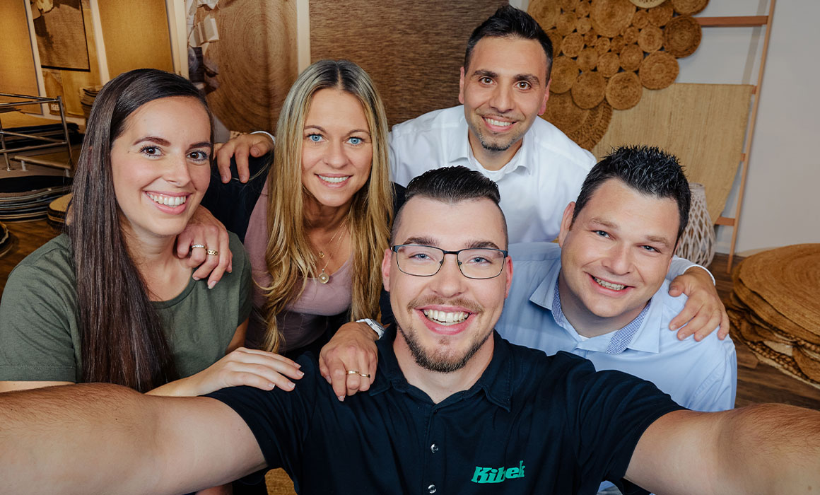 Fünf Personen lächeln in die Kamera und machen ein Gruppen-Selfie in Innenraum mit Dekoration.