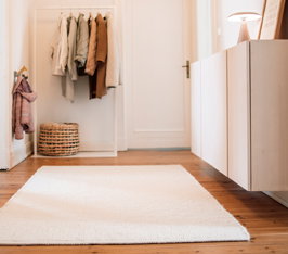 Heller Teppich liegt auf Holzboden in Flur mit Garderobe und weißen Schränken.