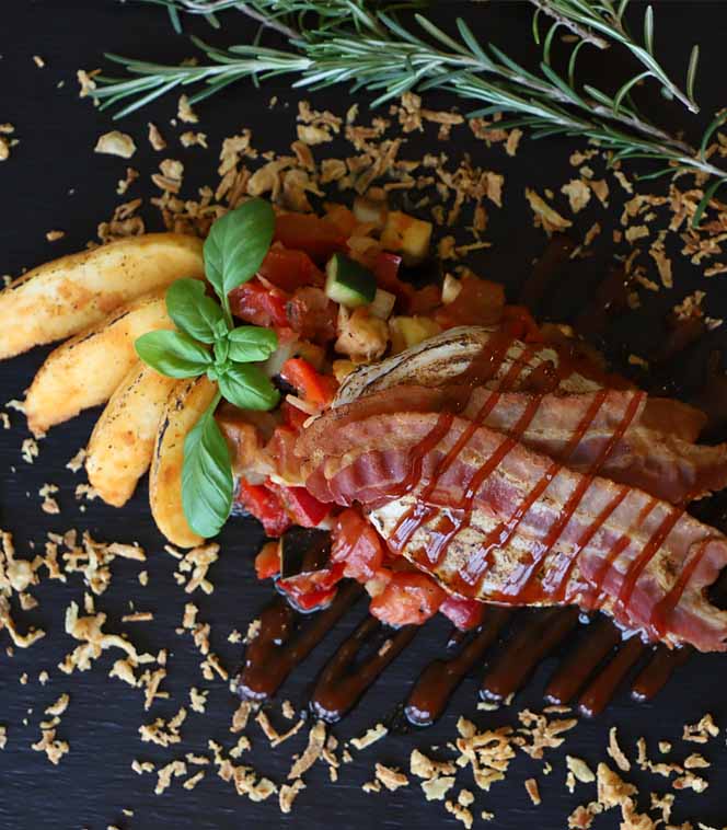 Gebratene Gnocchi und Gemüse mit Speck, Basilikum und Rosmarin auf schwarzem Teller serviert.