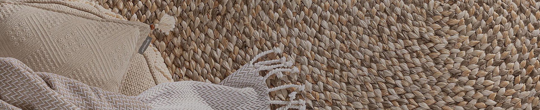 Zierkissen und Decke liegen auf einem geflochtenen Teppich mit natürlicher Textur.