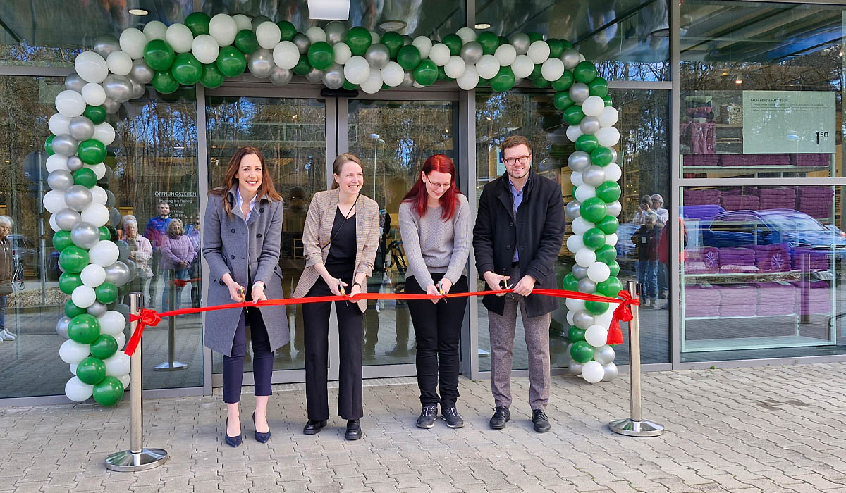 Vier Personen schneiden ein rotes Band vor einem Glasgebäude mit grün-weißem Luftballonbogen durch.