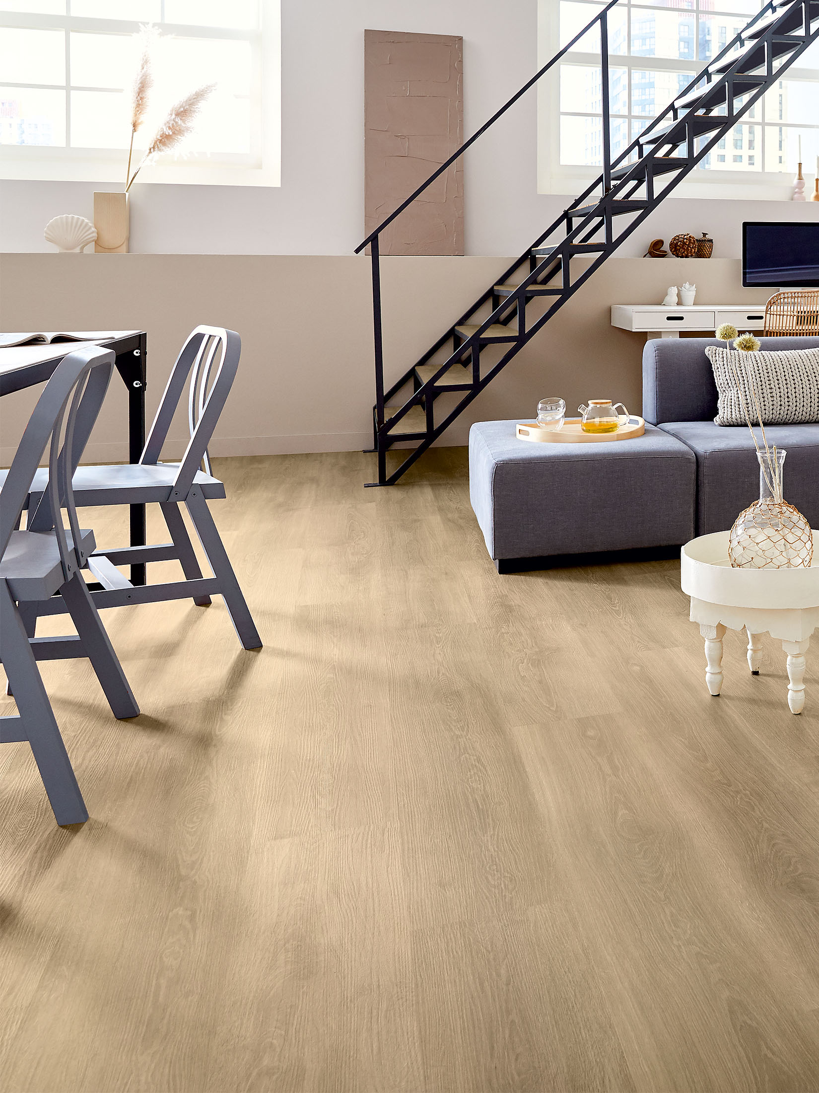 Treppe führt in einem hellen Wohnbereich mit Holzboden an Tisch und grauem Sofa vorbei