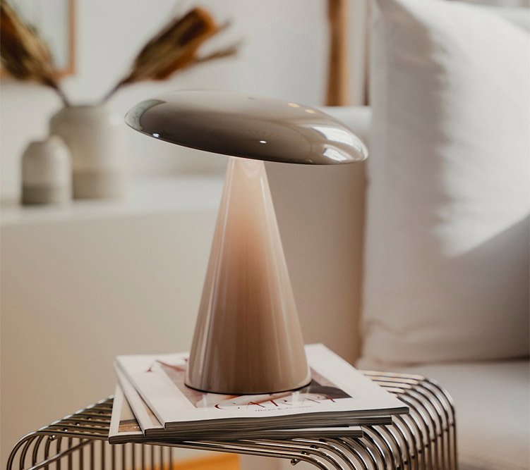Moderne Lampe steht auf Zeitschriften auf einem Metalltisch in einem Wohnzimmer mit Sofa.