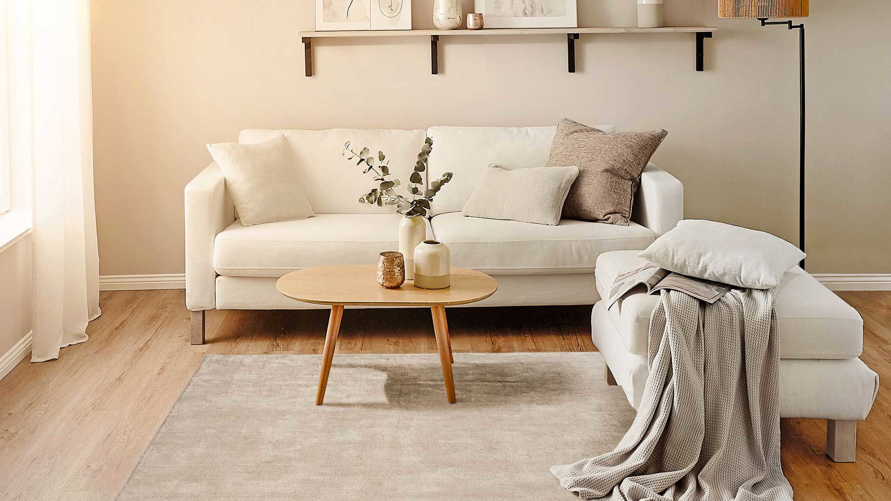 Sofa mit Kissen steht, Couchtisch mit Vasen davor, Tagesdecke und Buch liegen auf Hocker.