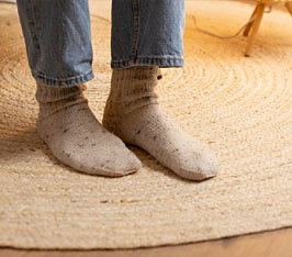 Füße in grauen Socken stehen auf einem runden, gewebten Teppich auf Holzboden.