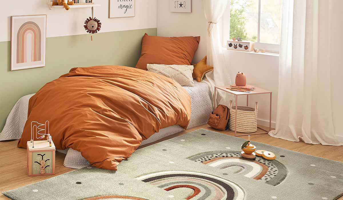 Kinderbett ist mit orangefarbenen Bettdecken bezogen, Spielzeug ist auf dem Teppich im Zimmer verteilt.