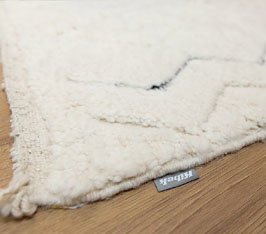 Teppich liegt auf Holzboden, zeigt Ecke mit Textiletikett „Kibek“ und feine Muster.