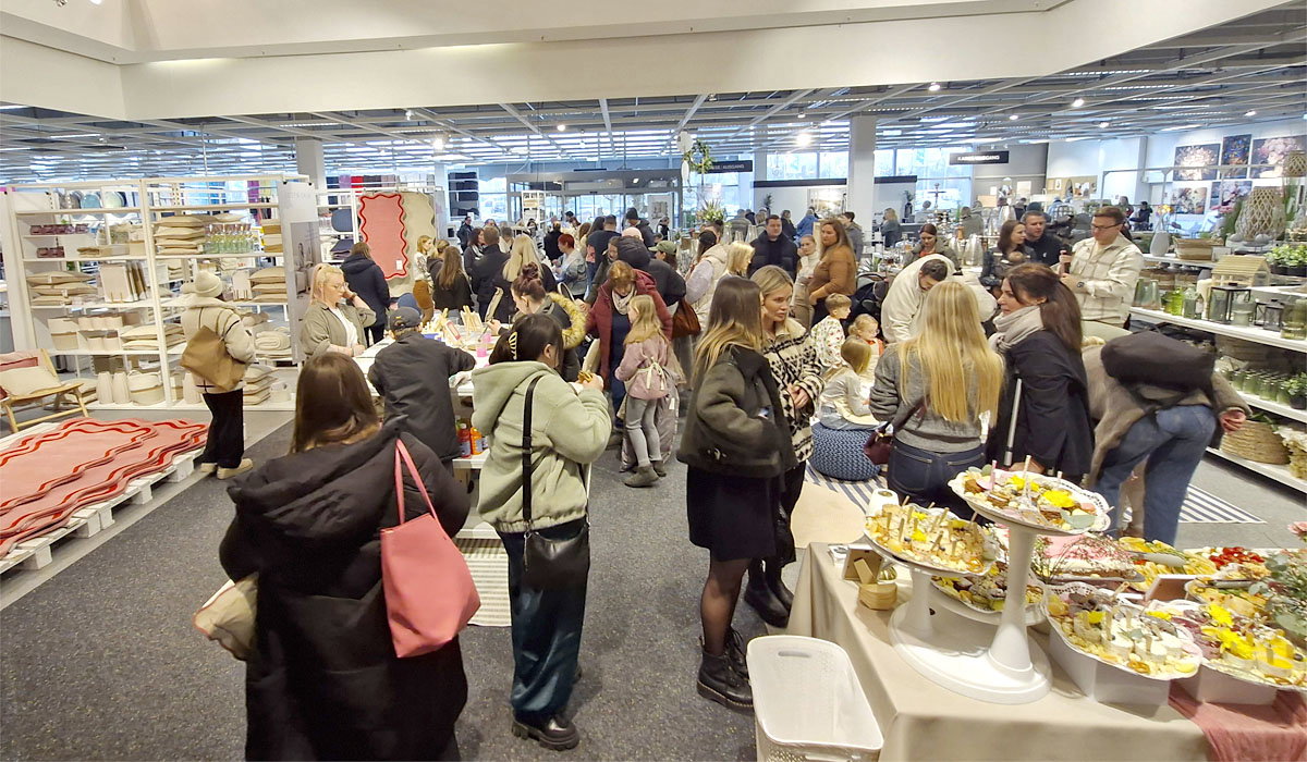 Menschen besuchen eine volle Ausstellung mit Dekoration, Essen und Haushaltswaren in Innenraum.