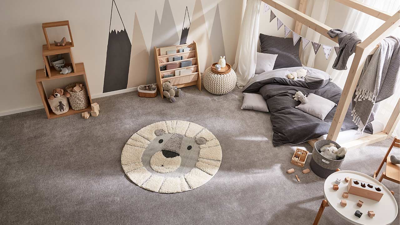 Kinderzimmer mit Tierteppich auf dem Boden, Spielzeug, Regal und niedrigen Betten in neutraler Farbgebung.