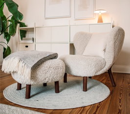 Sessel mit Hocker steht auf rundem Teppich in hellem Wohnzimmer mit Regal und Pflanze.