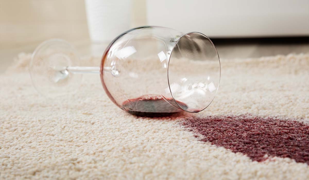 Weinglas liegt mit rot verschüttetem Wein auf hellem Teppich mit Muster.