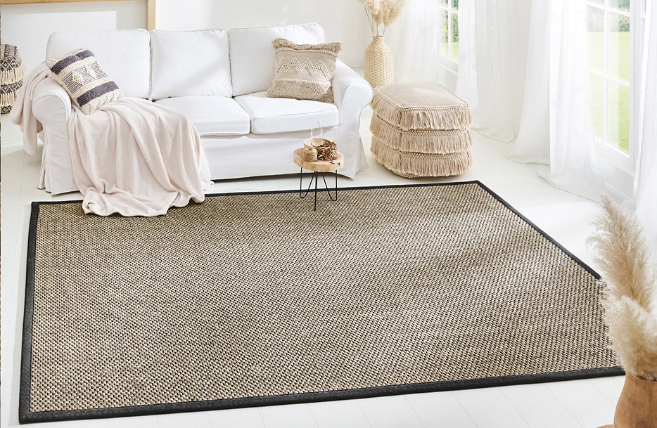 Teppich liegt flach vor einem weißen Sofa mit Kissen und Decke in hellem, sonnigem Wohnzimmer.