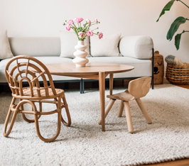 Vase mit rosa Blumen steht auf rundem Holztisch vor Sofagarnitur in hellem Raum.