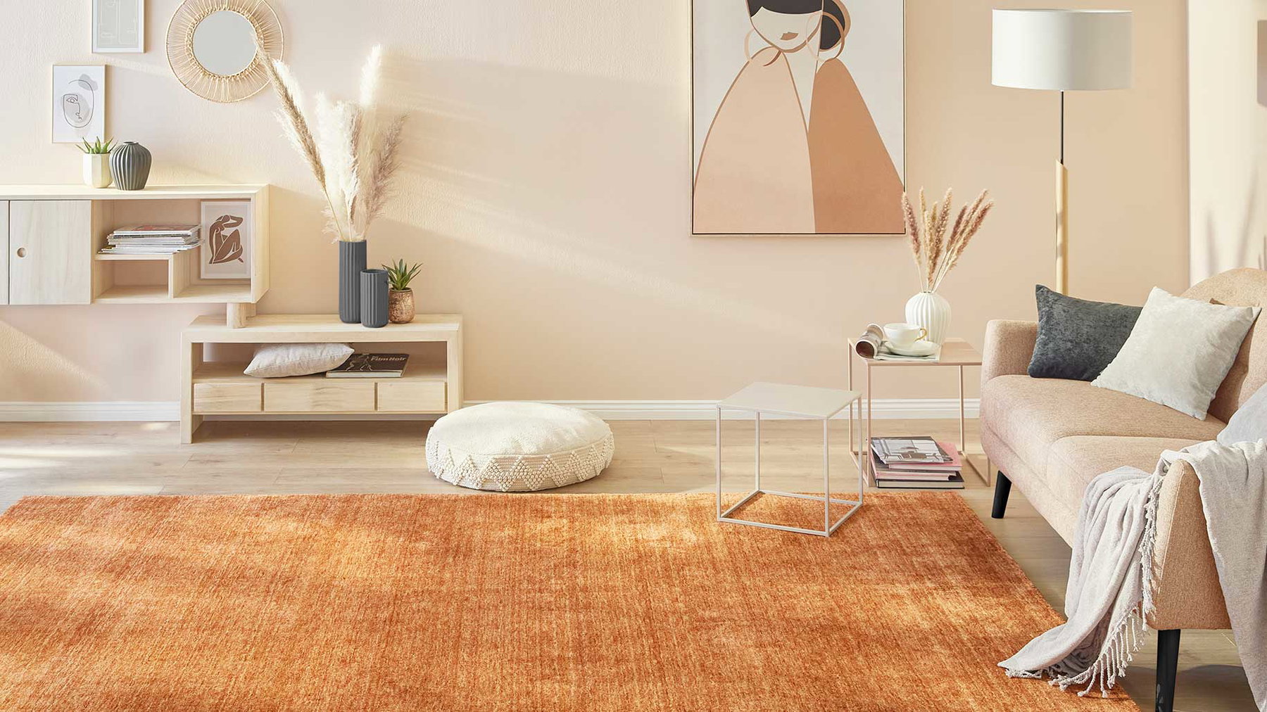 Wohnzimmer mit orangefarbenem Teppich, beige Couch, Tisch, Kissen, Pflanzen und Wandkunst.