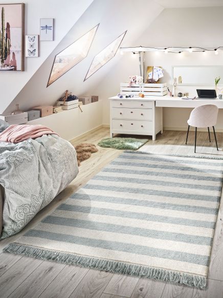 Gestreifter Teppich liegt auf Holzboden in hellem Schlafzimmer mit Schreibtisch und Bett.