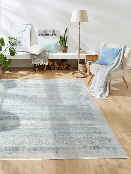 Blauer Teppich liegt auf Holzboden, daneben beige Sessel mit blauem Kissen und Lampe im Raum.