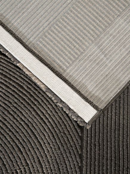 Teppich liegt auf strukturiertem Boden, obere Ecke des Teppichs hochgeklappt, helle und dunkle Farben.