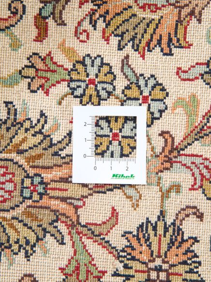 Maßstab liegt auf gewebtem Teppich mit floralem Muster in Beige, Rot, Blau und Grün.