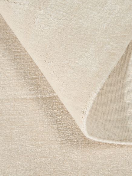 Beiger Teppich zeigt obere Ecke, die leicht umgeklappt ist, mit glatter Textur.