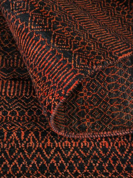 Teppich mit roten und schwarzen geometrischen Mustern, teilweise aufgerollt.