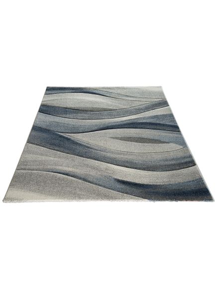 Teppich liegt flach mit wellenförmigem Muster in Blau- und Grautönen auf weißem Hintergrund.