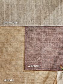 Drei verschiedenfarbige Teppiche Granit Grey, Aubergine und Mustard liegen auf Holzboden.